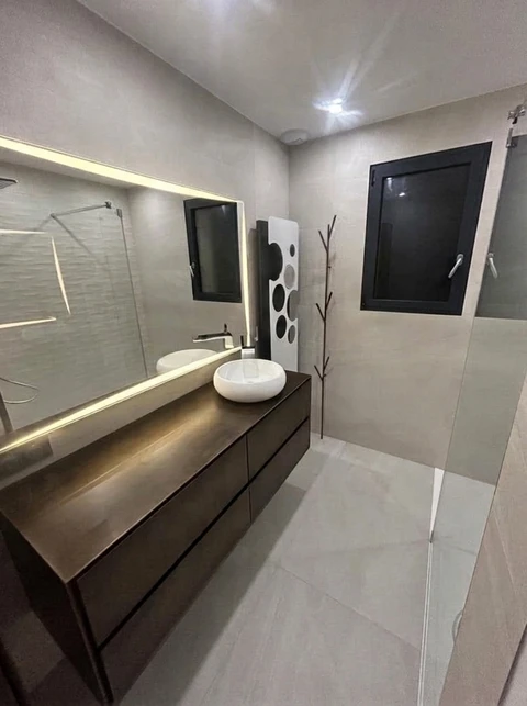 Salle de bain moderne avec vasque à poser ronde blanche sur meuble suspendu sombre à tiroirs, éclairé en LED