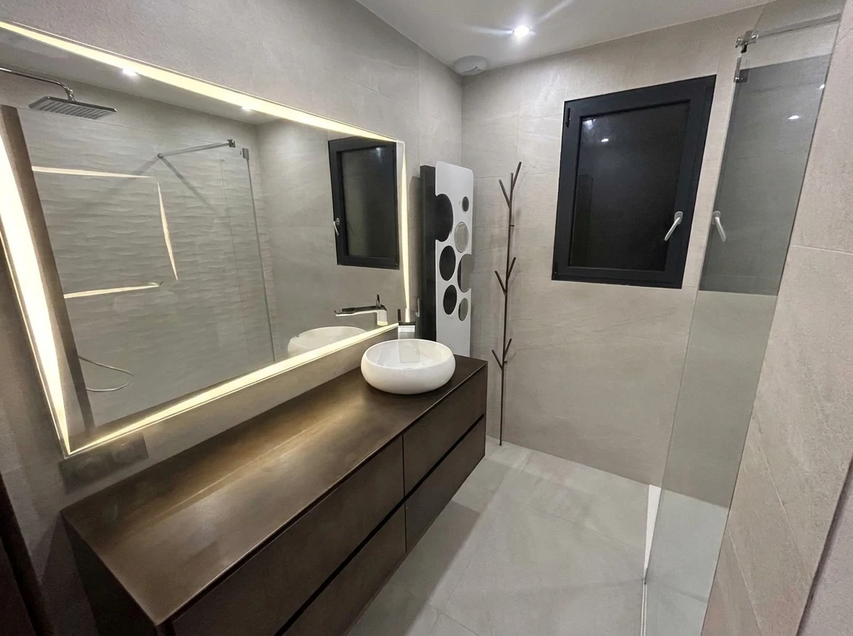 Salle de bain moderne avec douche à l'italienne, meuble vasque suspendu blanc, vasque à poser ronde, miroir encadré bois avec éclairage LED intégré, WC suspendu