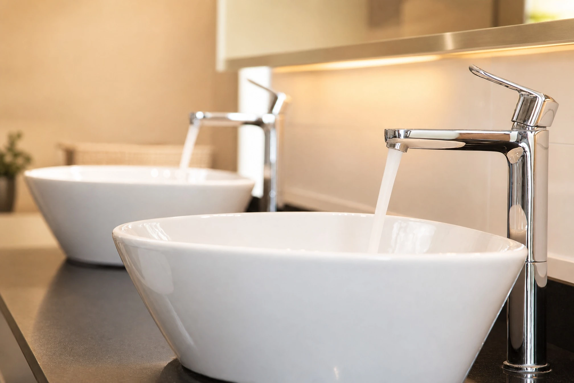 Salle de bain moderne avec deux vasques rondes blanches en céramique posées sur plan de travail sombre